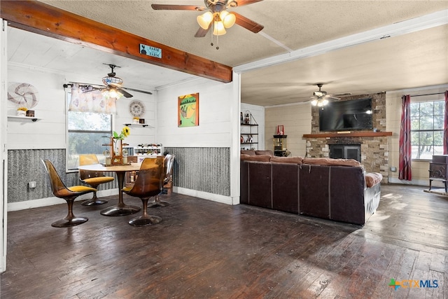 dining area featuring a stone fireplace, a textured ceiling, dark hardwood / wood-style flooring, wooden walls, and beamed ceiling