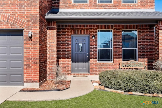 doorway to property with brick siding, roof with shingles, and an attached garage