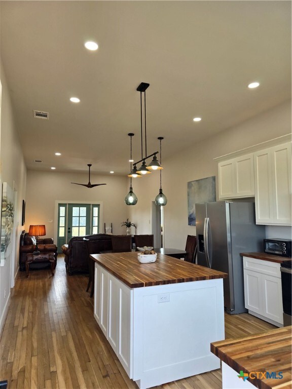 kitchen with visible vents, hanging light fixtures, white cabinets, a kitchen island, and butcher block countertops