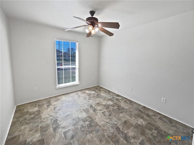 empty room featuring a ceiling fan, baseboards, and stone finish flooring