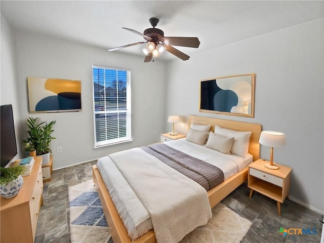 bedroom featuring ceiling fan, stone finish flooring, and baseboards