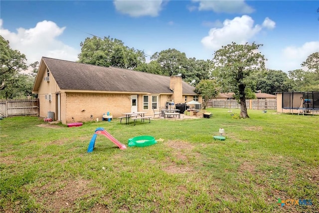 rear view of property featuring a lawn and a trampoline