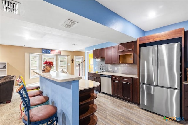 kitchen featuring stainless steel appliances, a kitchen breakfast bar, tasteful backsplash, light hardwood / wood-style floors, and a kitchen island