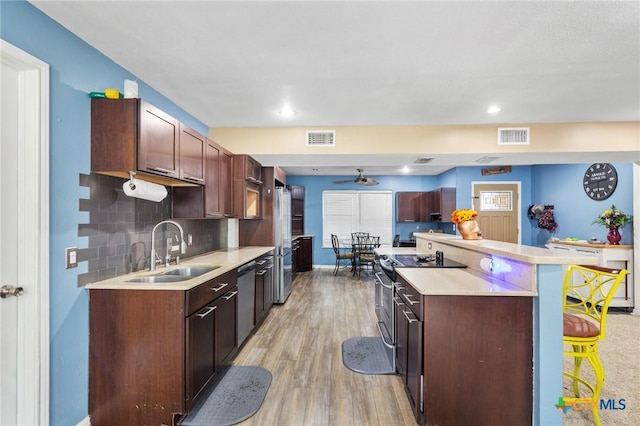 kitchen featuring ceiling fan, sink, stainless steel appliances, decorative backsplash, and a breakfast bar