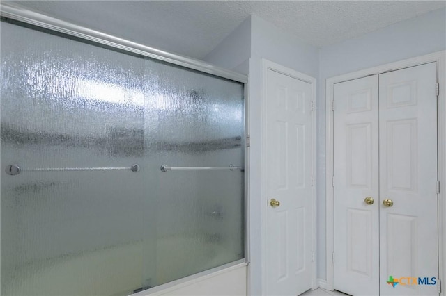 bathroom with a closet, bath / shower combo with glass door, and a textured ceiling