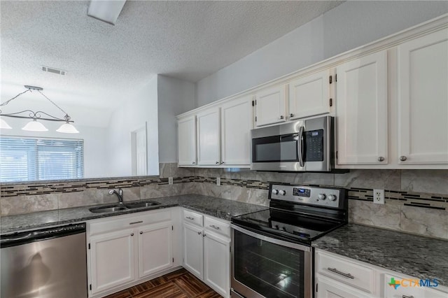 kitchen with white cabinetry, appliances with stainless steel finishes, dark stone counters, and a sink