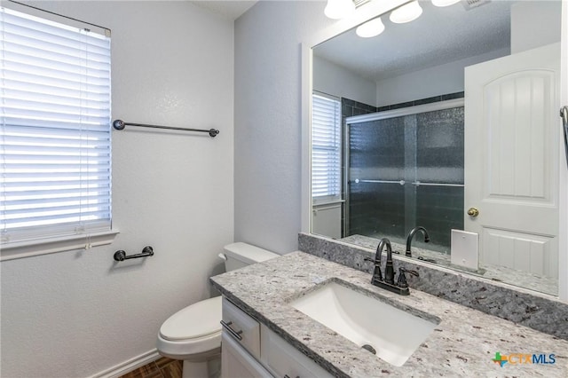 bathroom with a textured wall, tiled shower, vanity, and toilet