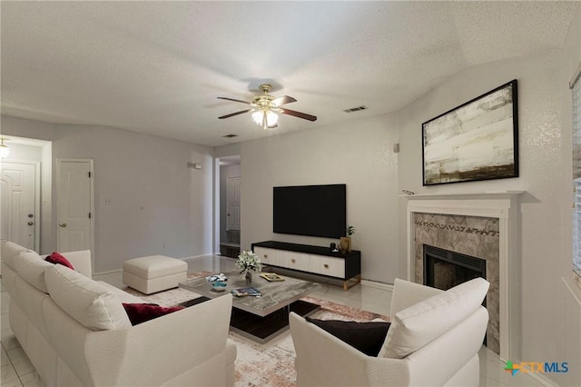 living room featuring a textured ceiling, a premium fireplace, visible vents, baseboards, and a ceiling fan