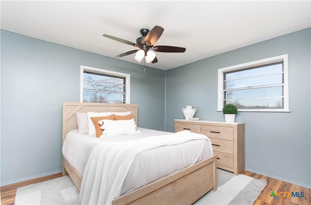 bedroom featuring baseboards, a textured ceiling, light wood-style flooring, and a ceiling fan