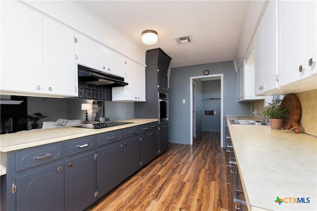 kitchen with oven, under cabinet range hood, light countertops, white cabinets, and black electric cooktop