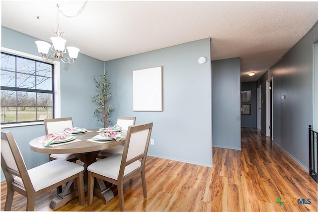 dining area with light wood-type flooring, baseboards, a notable chandelier, and a textured ceiling