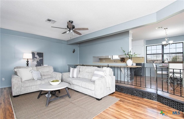 living area with visible vents, a textured ceiling, wood finished floors, and ceiling fan with notable chandelier