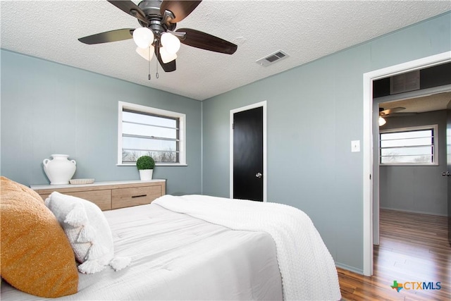 bedroom with visible vents, a textured ceiling, wood finished floors, baseboards, and ceiling fan