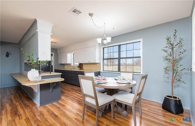 dining room with baseboards, visible vents, light wood-style floors, a textured ceiling, and a notable chandelier