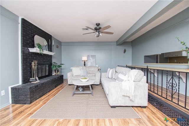 living area with visible vents, a brick fireplace, wood finished floors, a textured ceiling, and a ceiling fan