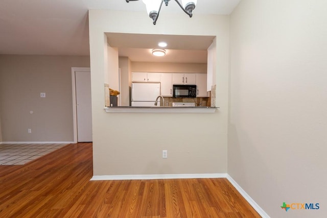 402 N Fredericksburg St Unit 9, San Marcos, TX 78666 - kitchen with black microwave, freestanding refrigerator, wood finished floors, white cabinetry, and tasteful backsplash