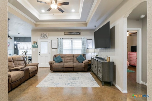 living room featuring a ceiling fan, a tray ceiling, concrete flooring, and ornamental molding