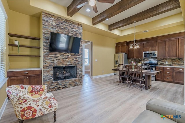 living area featuring beamed ceiling, a fireplace, baseboards, and light wood finished floors