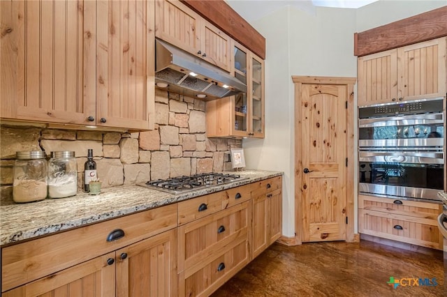 kitchen featuring light stone countertops, light brown cabinets, decorative backsplash, appliances with stainless steel finishes, and under cabinet range hood