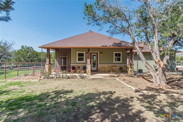 back of house featuring stucco siding, a lawn, stone siding, fence, and covered porch