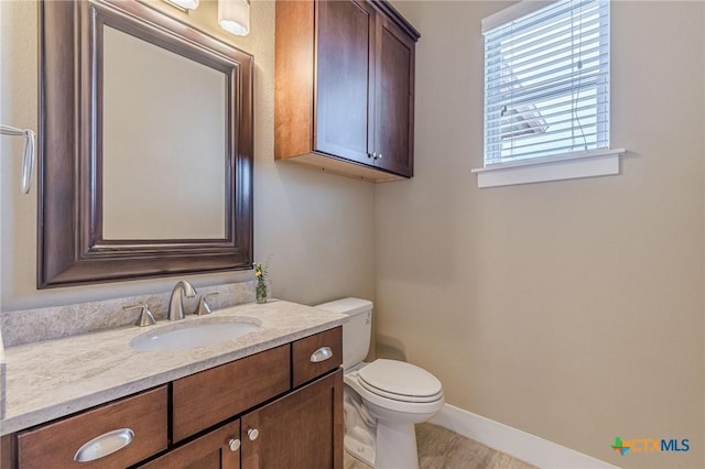 half bath featuring vanity, toilet, and baseboards