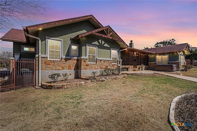 view of front of home featuring fence, a sunroom, stucco siding, stone siding, and a lawn