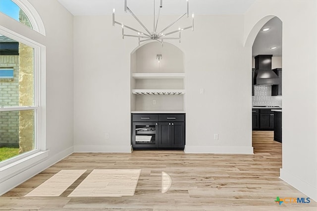 unfurnished dining area featuring built in shelves, light hardwood / wood-style flooring, and a chandelier