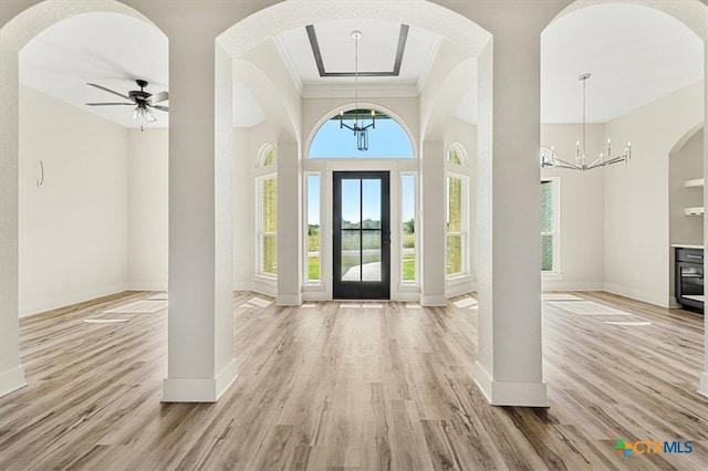 foyer with light wood-type flooring, a raised ceiling, ornamental molding, and ceiling fan with notable chandelier