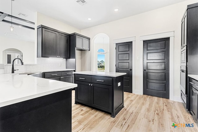 kitchen with light hardwood / wood-style floors, light stone counters, decorative backsplash, sink, and pendant lighting