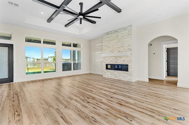 unfurnished living room featuring a stone fireplace, coffered ceiling, beamed ceiling, ceiling fan, and light hardwood / wood-style flooring