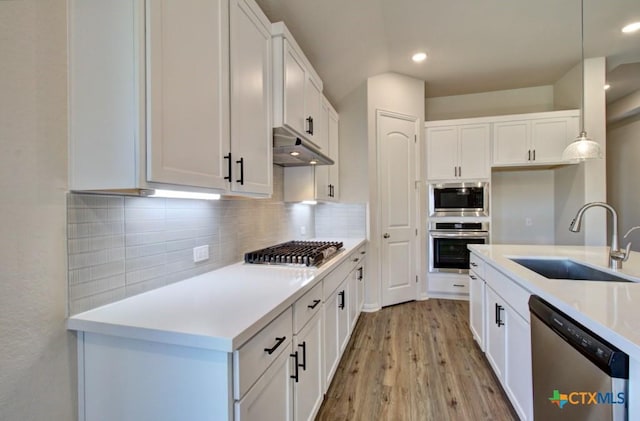 kitchen with a sink, appliances with stainless steel finishes, light wood-style flooring, backsplash, and under cabinet range hood