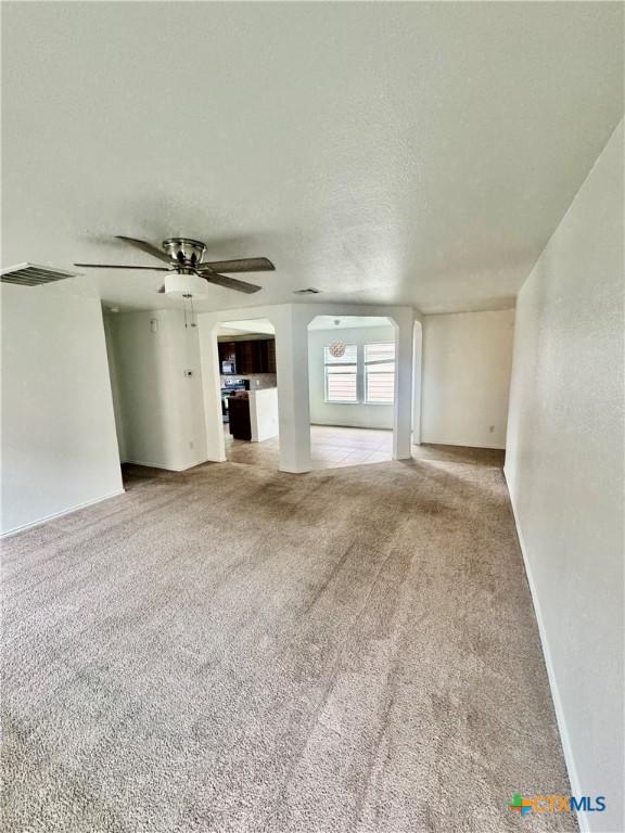 unfurnished living room featuring visible vents, arched walkways, ceiling fan, carpet, and a textured ceiling