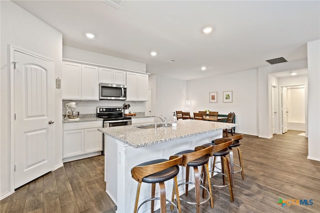 1004 Norway Dr, Seguin, TX 78155 - kitchen with stainless steel appliances, a kitchen breakfast bar, dark wood-style flooring, white cabinets, and recessed lighting