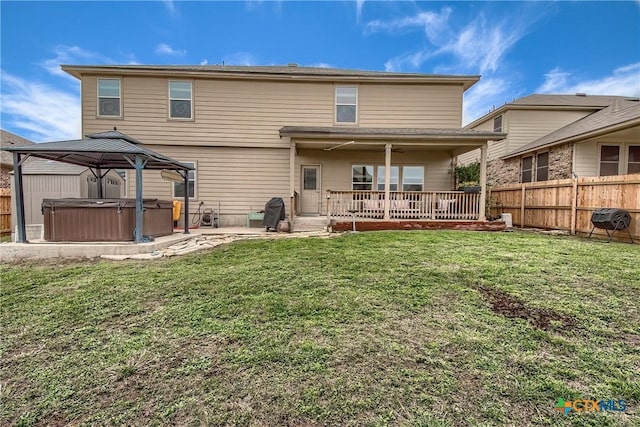 rear view of property with a lawn, a patio area, a fenced backyard, and a hot tub