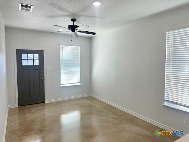 foyer entrance featuring finished concrete flooring, visible vents, ceiling fan, a textured ceiling, and baseboards