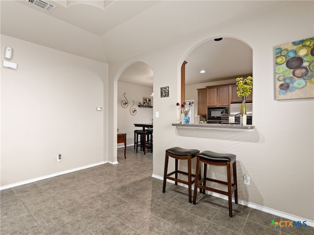 9823 Amberg Path, Helotes, TX 78023 - kitchen featuring black microwave, arched walkways, a breakfast bar area, freestanding refrigerator, and dark tile patterned flooring