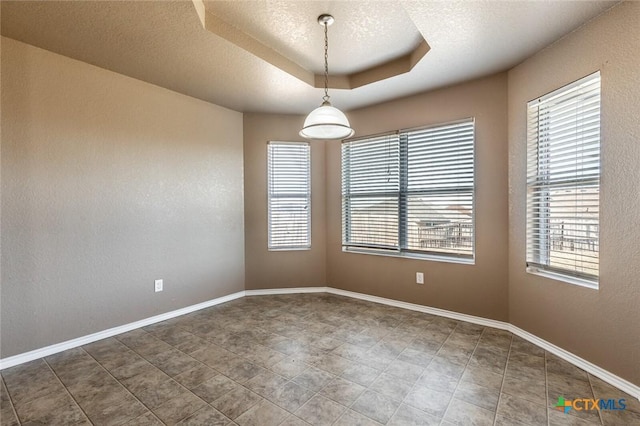 empty room featuring plenty of natural light, a raised ceiling, and a textured ceiling