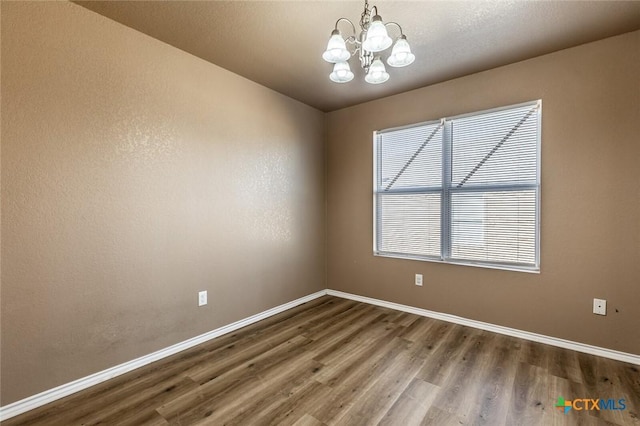 spare room with hardwood / wood-style flooring and a chandelier