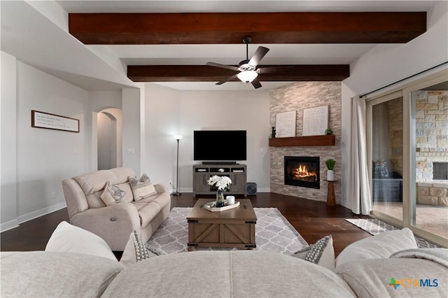 living room featuring a fireplace, beam ceiling, dark wood-type flooring, and ceiling fan