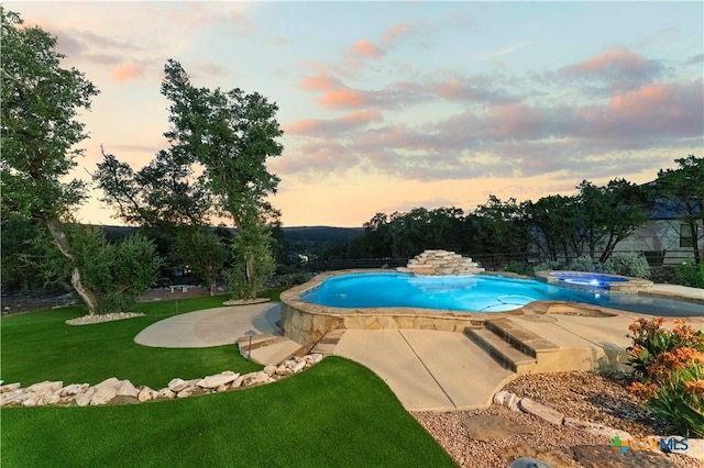 pool at dusk featuring an in ground hot tub, a patio area, and a lawn