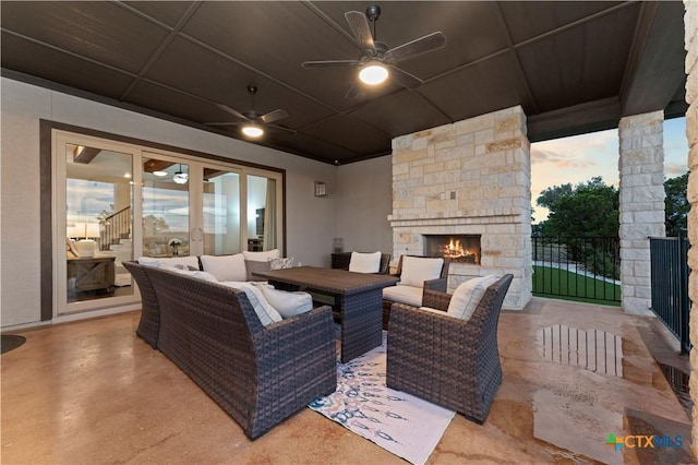 patio terrace at dusk featuring ceiling fan and an outdoor stone fireplace