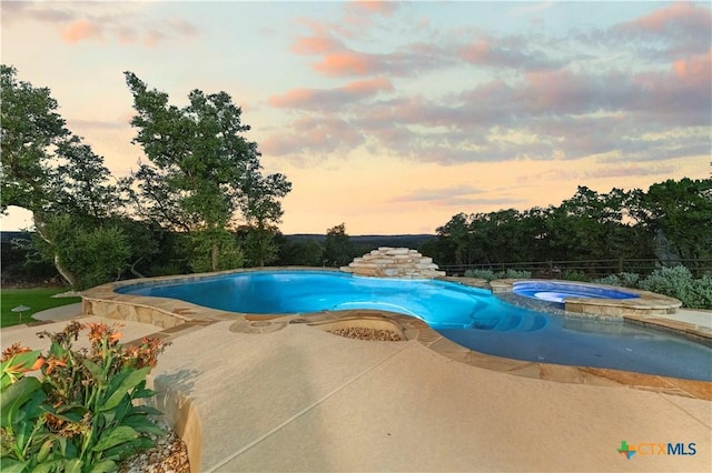 pool at dusk featuring a patio and an in ground hot tub