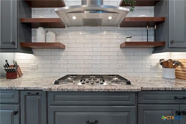 kitchen with light stone counters, island range hood, stainless steel gas stovetop, and backsplash