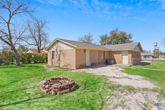 back of property with fence, a fire pit, central air condition unit, a lawn, and brick siding