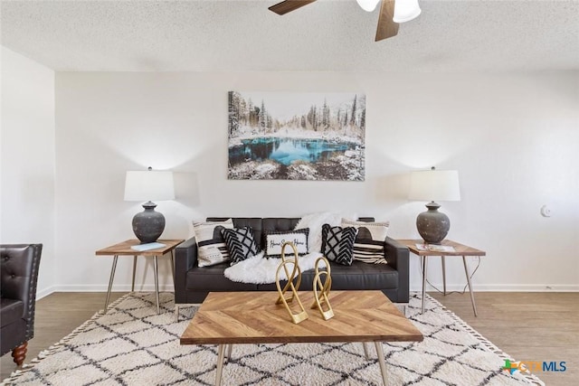 living area with ceiling fan, a textured ceiling, and wood finished floors