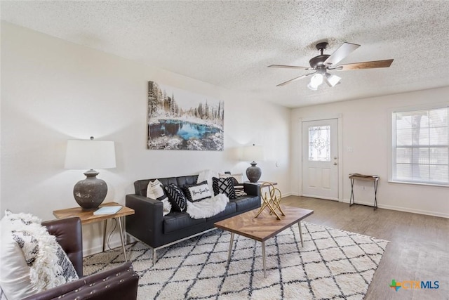 living room with wood finished floors, a ceiling fan, baseboards, and a textured ceiling