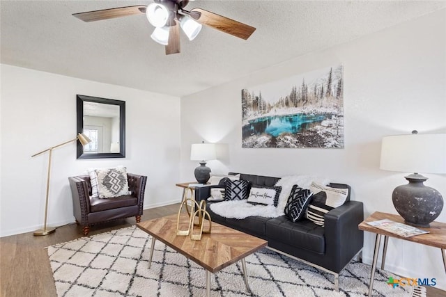 living area featuring baseboards, a textured ceiling, wood finished floors, and a ceiling fan