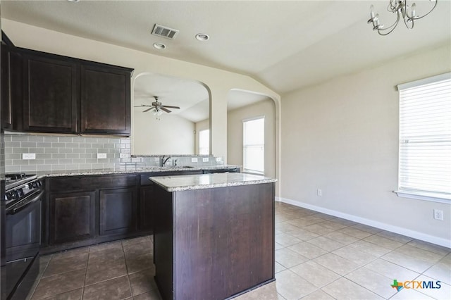 kitchen featuring lofted ceiling, black range with gas cooktop, a center island, light stone countertops, and backsplash