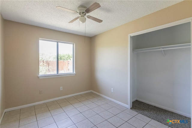 unfurnished bedroom featuring a textured ceiling, light tile patterned floors, ceiling fan, and a closet