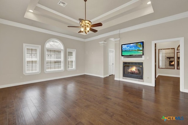 unfurnished living room featuring dark wood-type flooring, ceiling fan, ornamental molding, and a tray ceiling